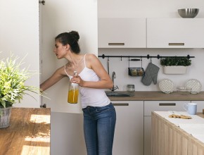 Side view of woman holding bottle of juice while looking in frid